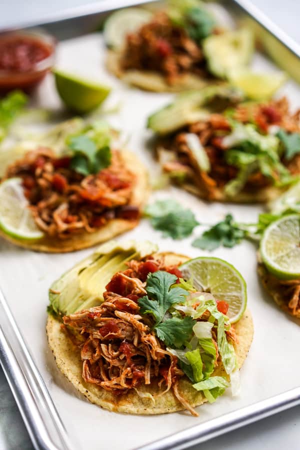 Tostadas topped with shredded chipotle chicken, avocados, cilantro, lettuce and a wedge of lime