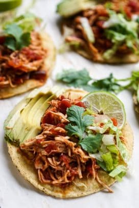 Tostadas topped with shredded chipotle chicken, avocados, cilantro, lettuce and a wedge of lime