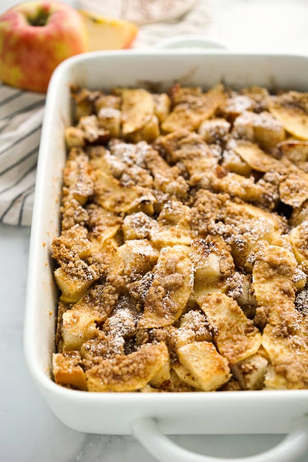 French Toast Casserole topped with sliced apples and powdered sugar in a rectangular dish