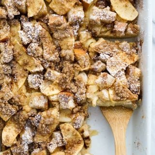 Using a spatula to lift up a square slice of Baked French Toast Casserole from a rectangular dish.