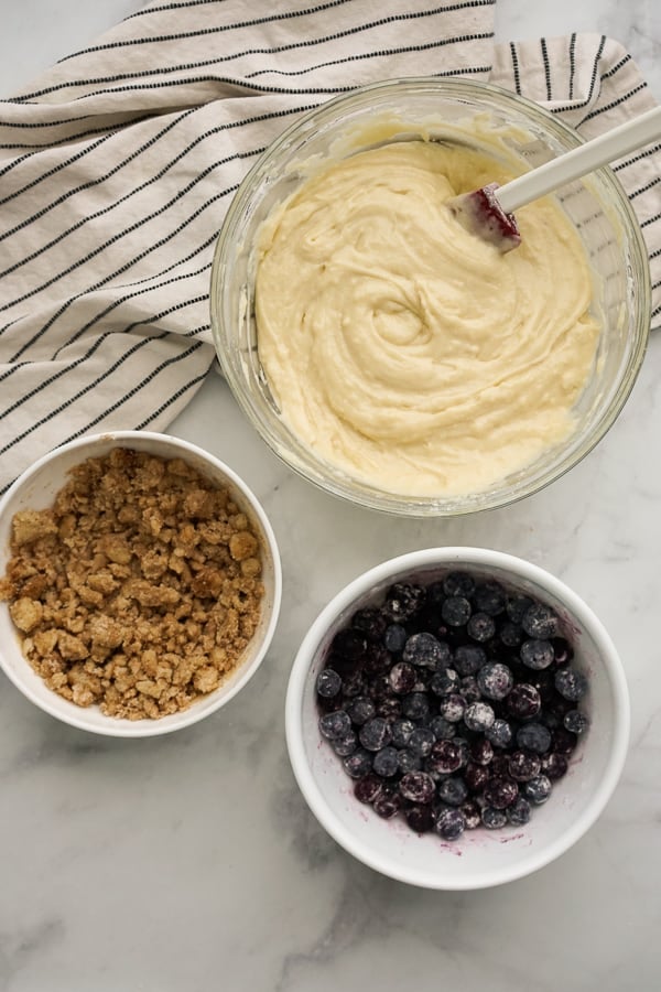 Three bowls, each filled with blueberry bread mixture, crumble topping and blueberries