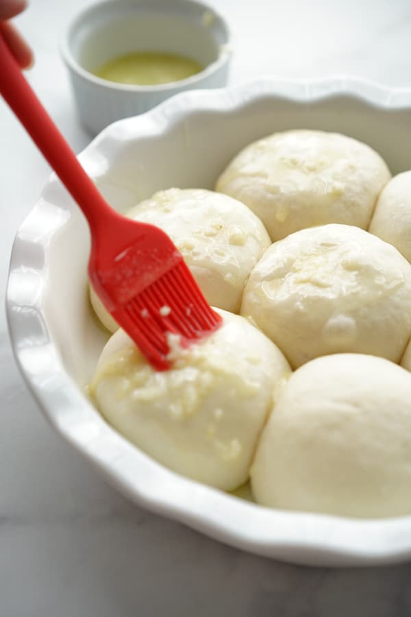 Brushing garlic butter onto risen bread dough