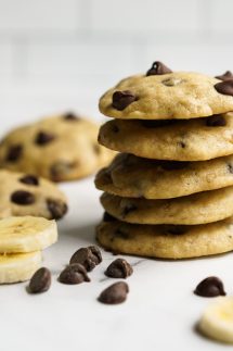 A stack of cookies loaded with chocolate chips, with more chocolate chips and banana slices around it