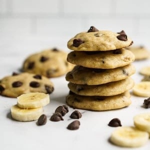 A stack of cookies loaded with chocolate chips, with more chocolate chips and banana slices around it