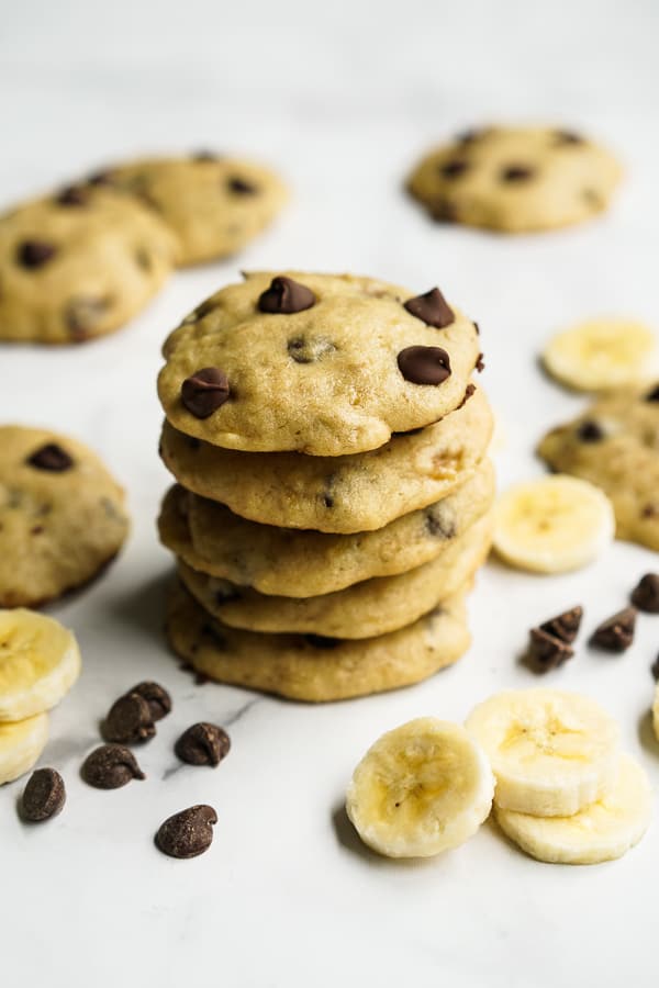 A stack of cookies with more cookies, sliced bananas and chocolate chips around it