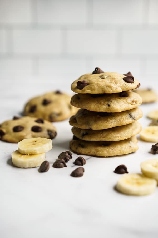 A tall stack of Banana Chocolate Chip Cookies with banana and chocolate chips around it