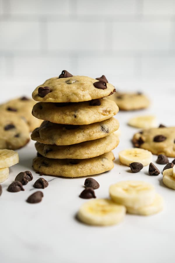 A tall stack of cookies with banana and chocolate chips around it