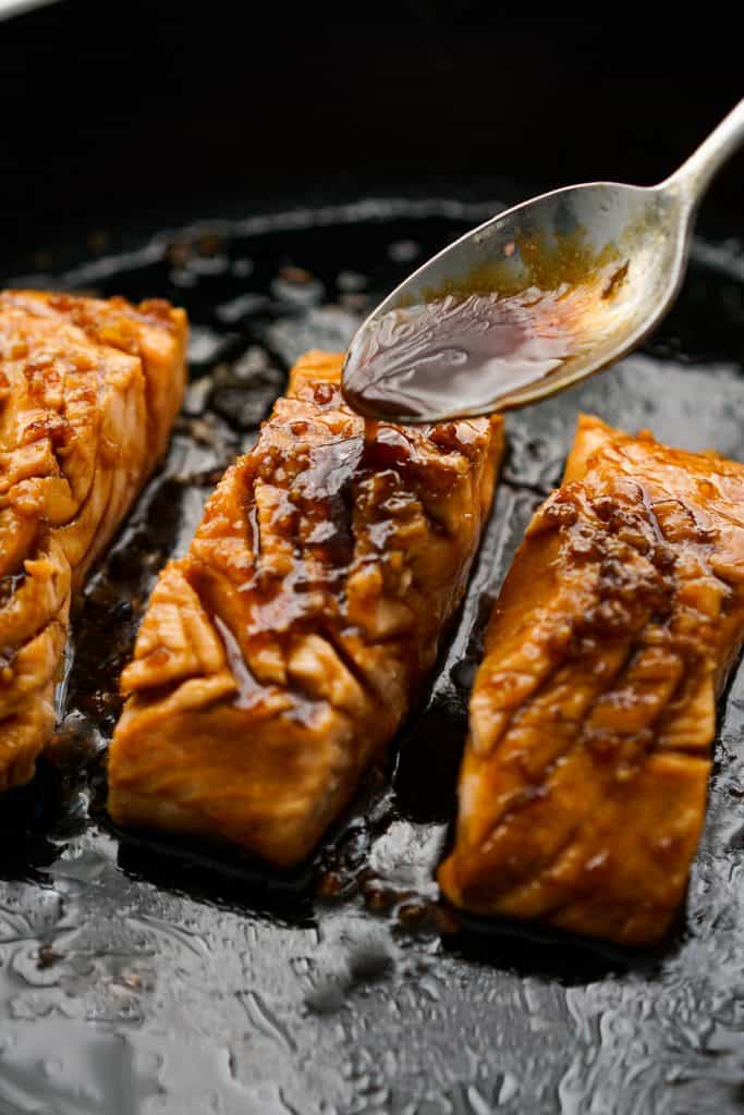 Drizzling teriyaki sauce onto salmon on skillet