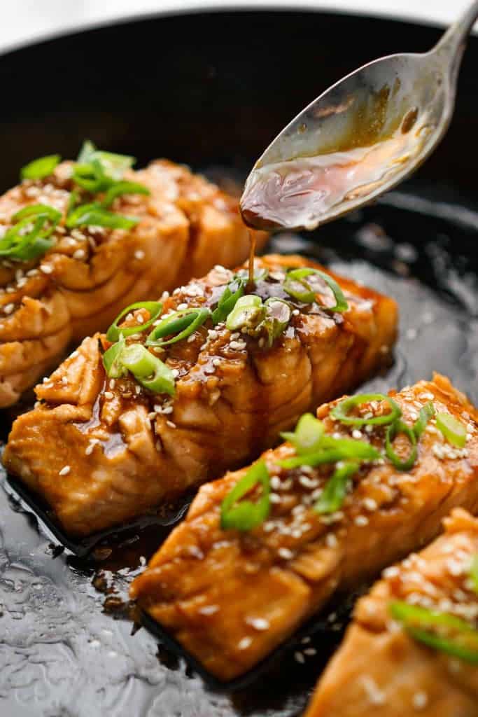 Drizzling teriyaki sauce onto salmon in a skillet