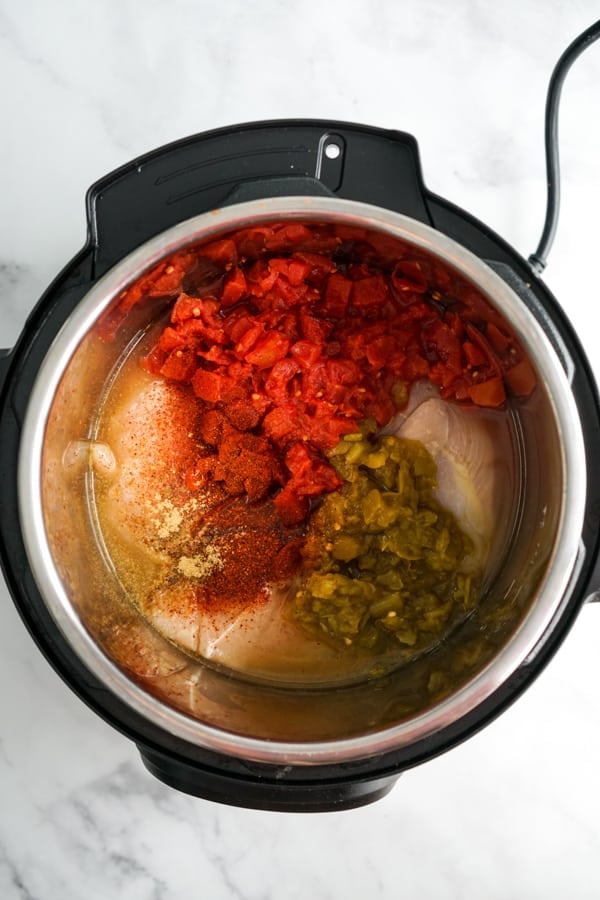 Uncooked chicken, tomatoes, spices, green chilis and chicken broth in the Instant Pot