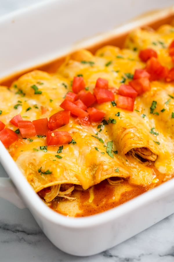 Closeup of chicken enchiladas topped with diced tomatoes
