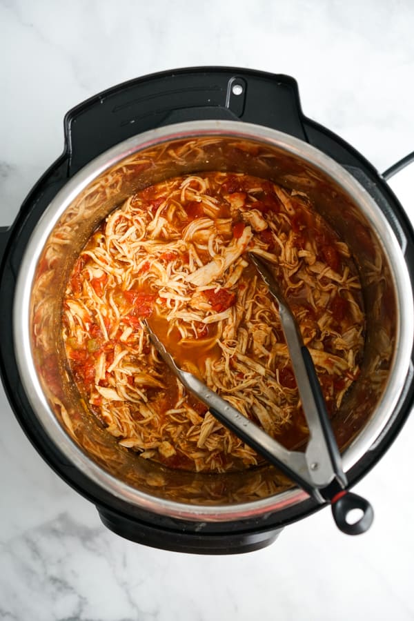 Shredded cooked chicken in the Instant Pot with a pair of tongs