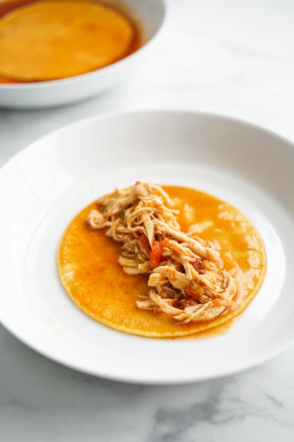 Adding shredded chicken to the middle of corn tortilla