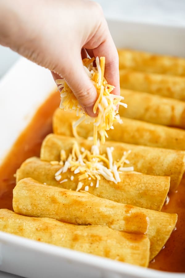 Adding shredded cheese to enchiladas