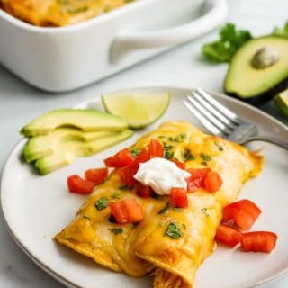 A plate filled with two chicken enchilada, with a casserole of chicken enchiladas in the background