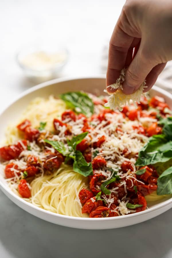 Sprinkling shredded parmesan onto a bowl of pasta