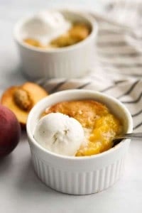 Peach cobbler in small ramekin topped with vanilla ice cream