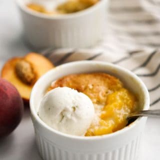 Peach cobbler in small ramekin topped with vanilla ice cream