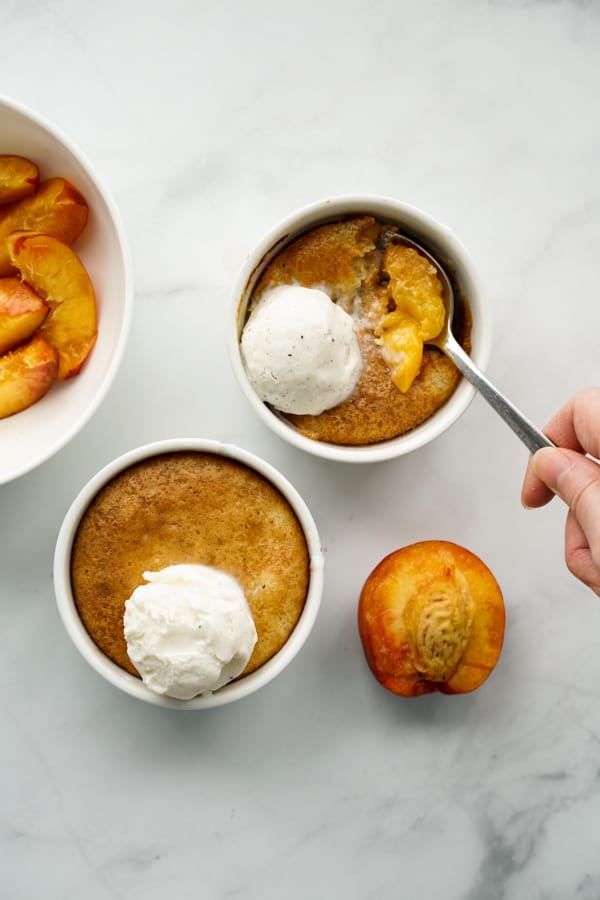 Two ramekins of peach cobbler with ice cream on top, a spoon digging into one of them