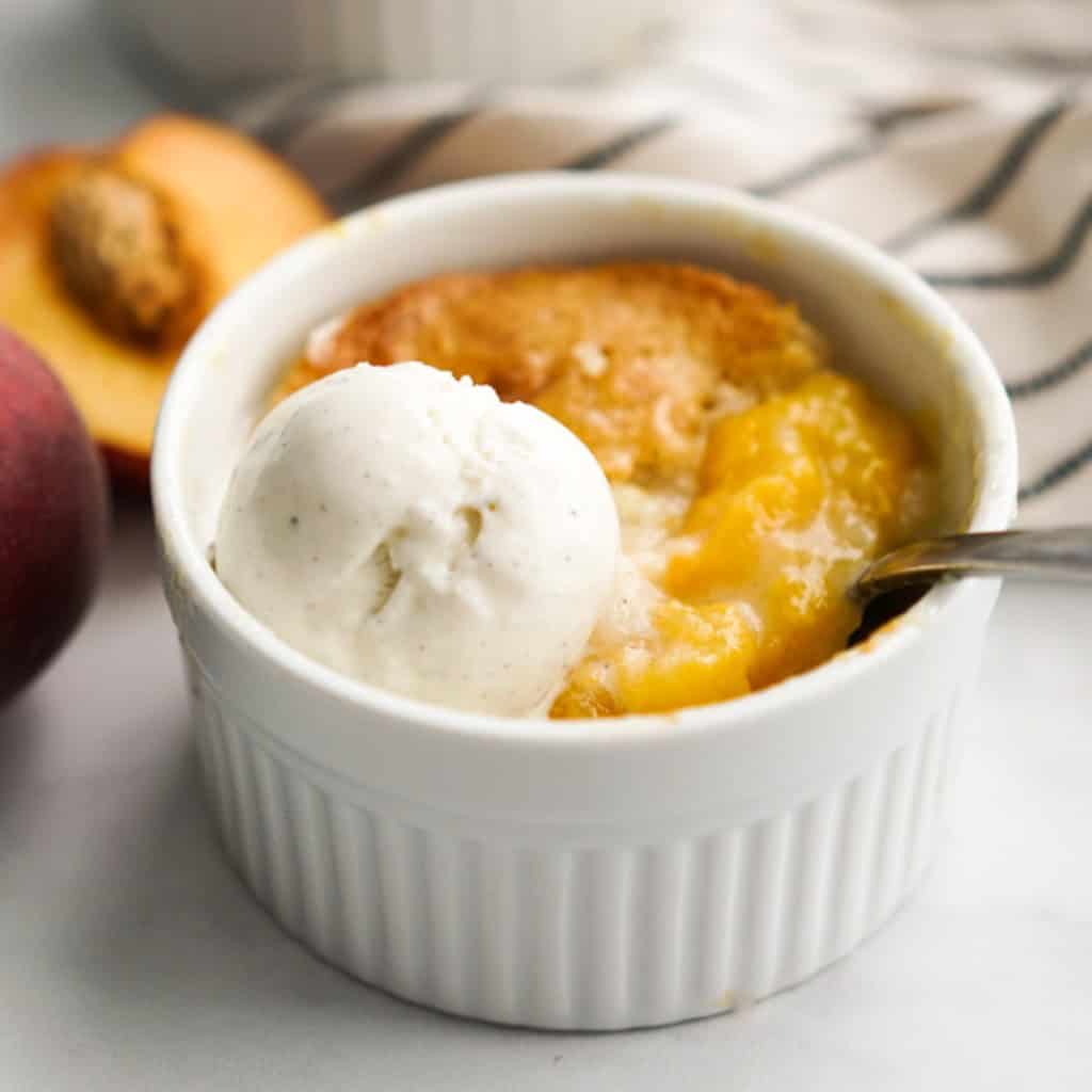 A single serve peach cobbler in a ramekin topped with ice cream