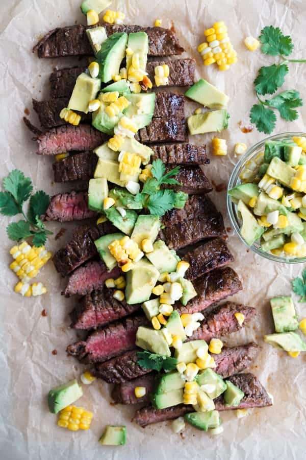 Sliced marinated flank steak topped with avocado corn pieces