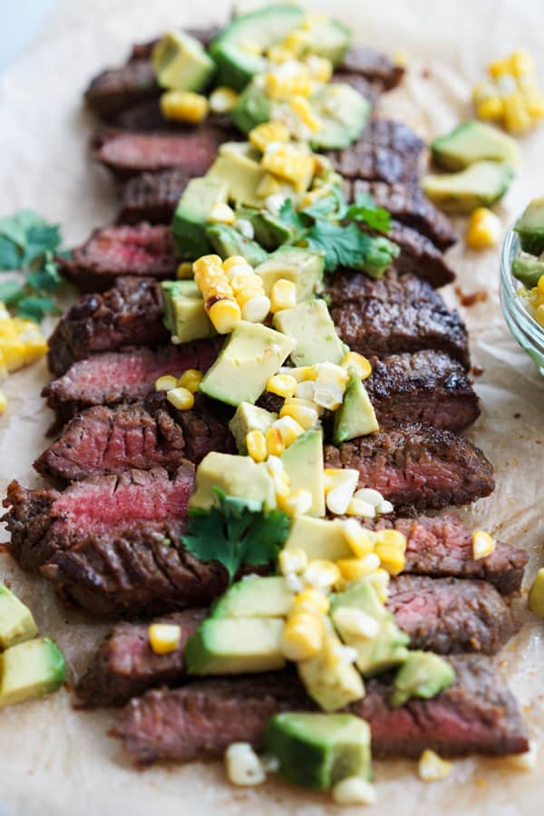 Sliced flank steak in strips topped with avocado and corn pieces