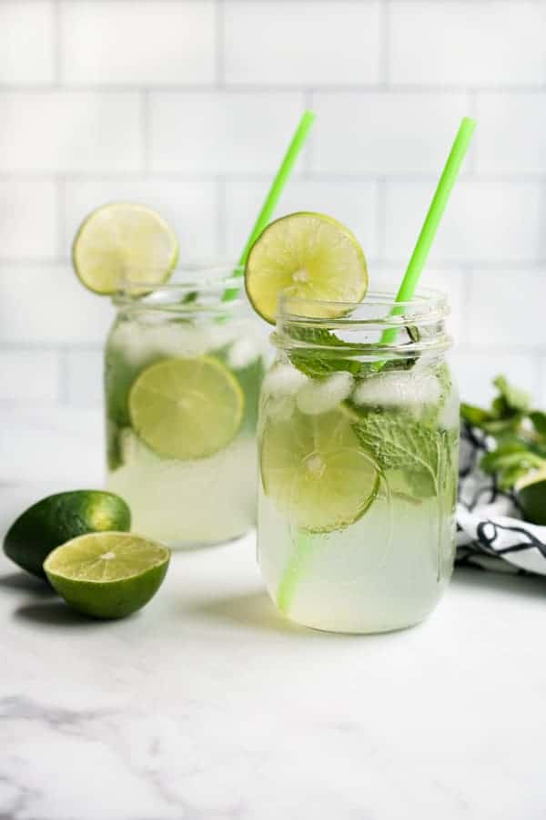 Two mason jars of mojito mocktails filled with lime and mint leaves, with slices of lime next to them.