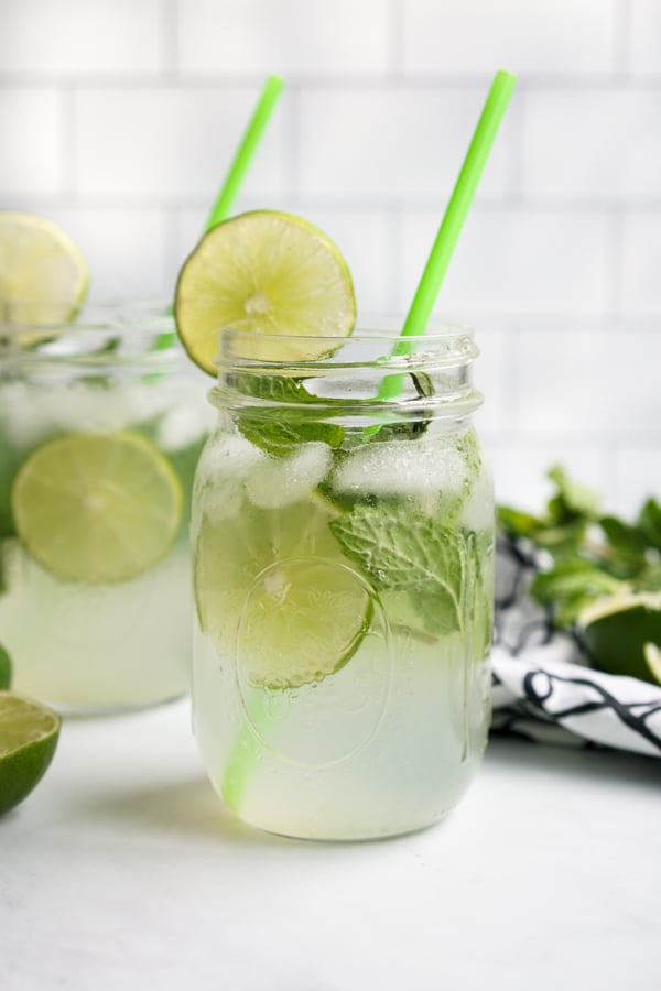 Two mason jars filled with mojito mocktail, lime slices and mint leaves.