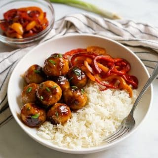 A bowl of sweet and sour meatballs, rice and bell peppers, with a fork in the bowl