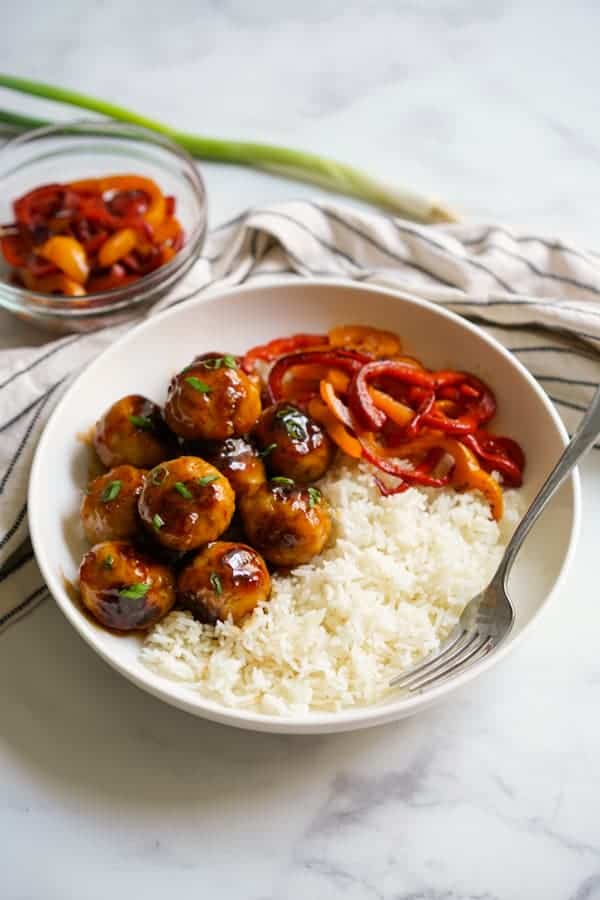 A bowl of sweet and sour meatballs, rice and bell peppers, with a fork in the bowl