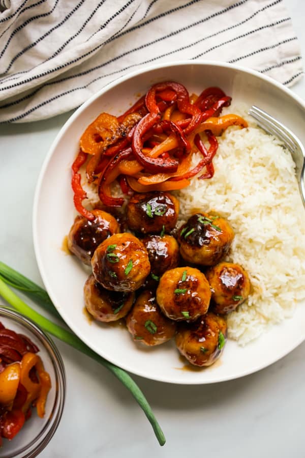 A bowl of chicken meatballs coated in sweet and sour sauce, rice and bell peppers