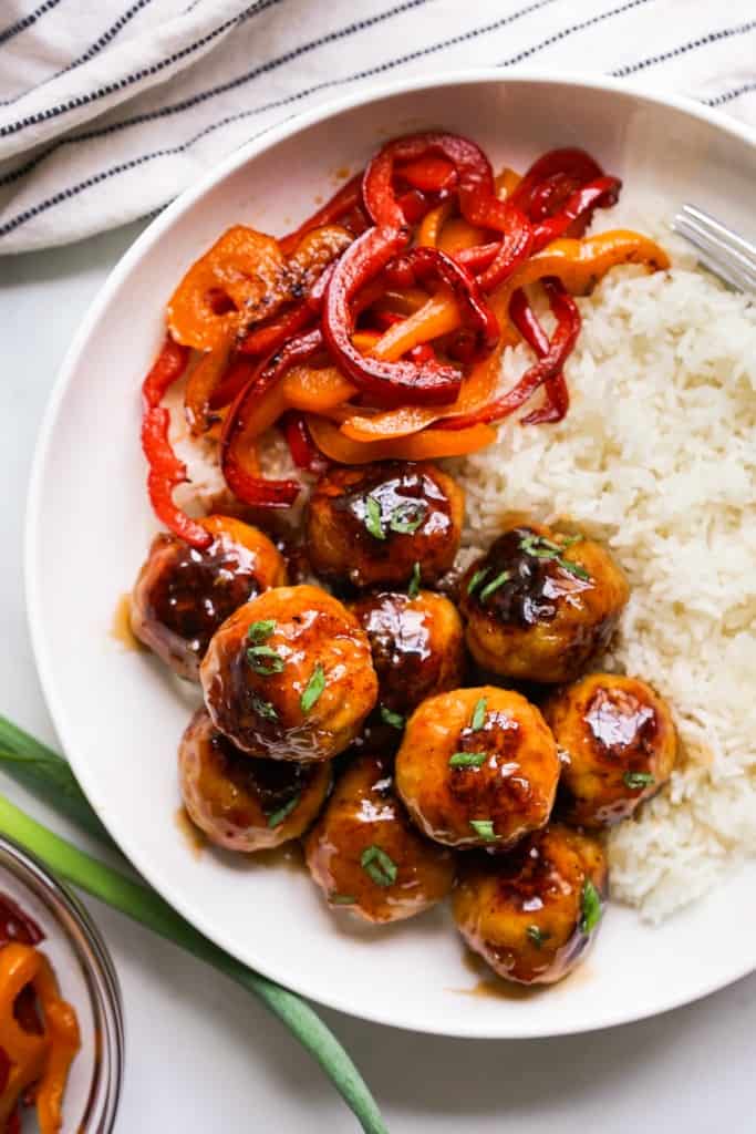 A plate of rice, bell peppers and sweet and sour meatballs