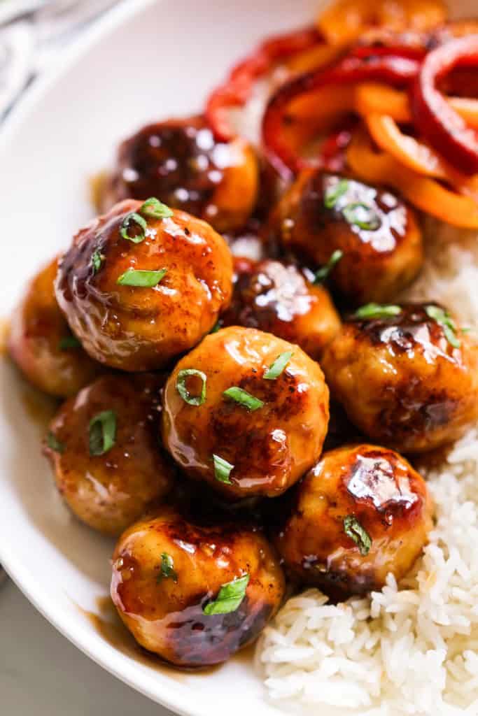 Closeup of sweet and sour meatballs with sauted bell peppers in the background