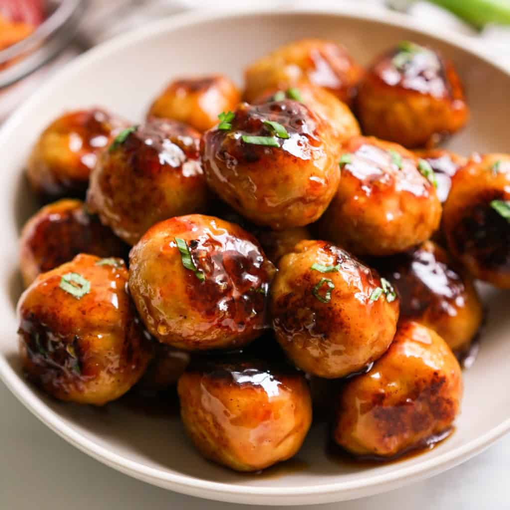 A bowl of meatballs piled on top of each other coated in sweet and sour sauce