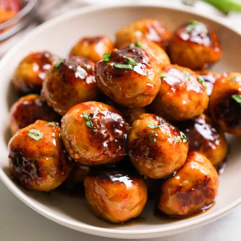 A bowl of meatballs piled on top of each other coated in sweet and sour sauce