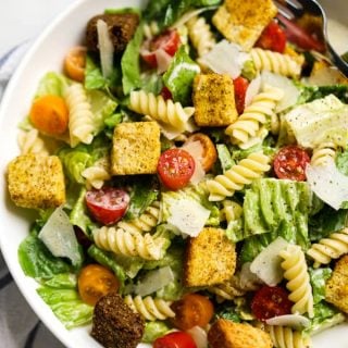 Closeup of a bowl filled with lettuce, rotini pasta, tomatoes, parmesan and croutons