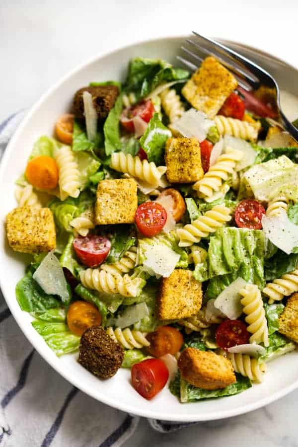 Closeup of a bowl filled with lettuce, rotini pasta, tomatoes, parmesan and croutons