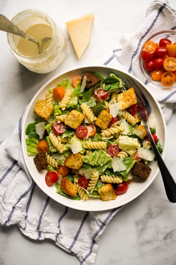 Top down picture of lettuce, tomatoes, croutons, parmesan with Caesar dressing on the side