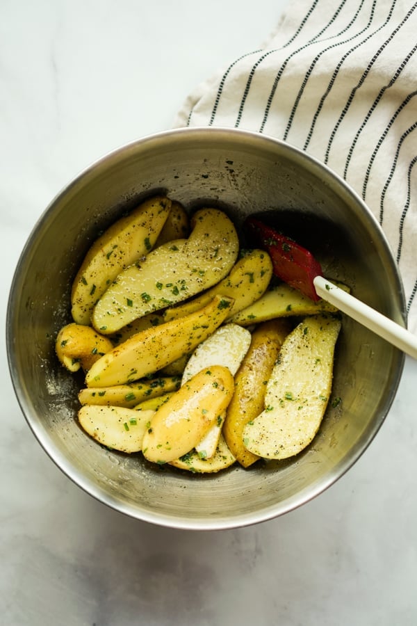 Raw fingerling potatoes tossed in herbs in a large bowl
