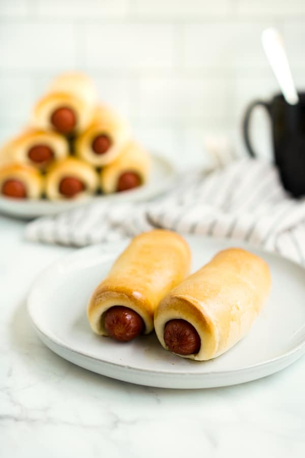 A plate of two sausage kolaches with more sausage kolaches in the background