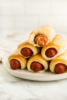 A stack of sausage rolls with one that is already bite into on the top of the stack