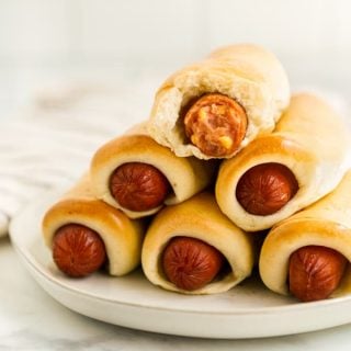 A stack of sausage rolls with one that is already bite into on the top of the stack
