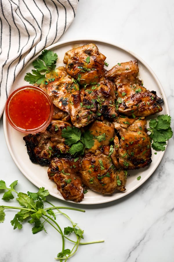 A round plate of Thai Grilled Chicken with a small bowl of sauce on the side