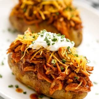 Two baked russet potatoes topped with shredded BBQ chicken, shredded cheddar cheese, sour cream, and chives