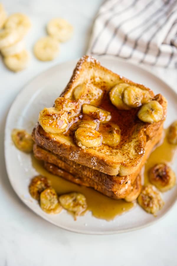 A stack of french toast topped with caramelized bananas and maple syrup