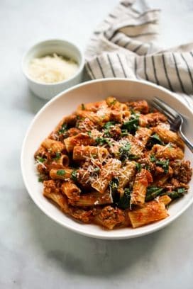 A bowl of rigatoni pasta coated in creamy tomato sauce, combined with Italian sausage and spinach