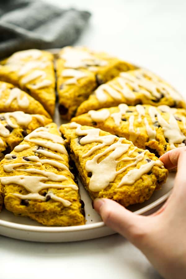 Hand grabbing a slice of triangular pumpkin scone with chocolate chips.