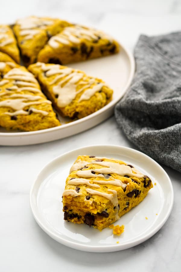 A plate of half eaten pumpkin chocolate chip scones with more scones in the background