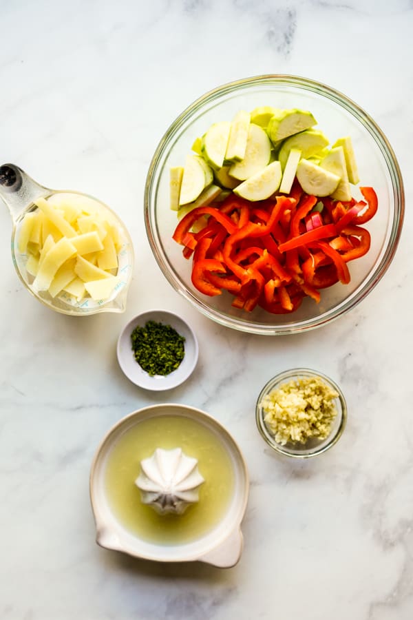 A large bowl of zucchini and bell peppers, a measuring cup filled with water chestnuts, lime juice, ginger, garlic, and lime zest