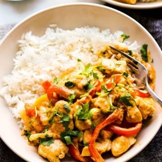Close up of a bowl of rice topped with Thai curry with chicken, bell peppers and zucchini.
